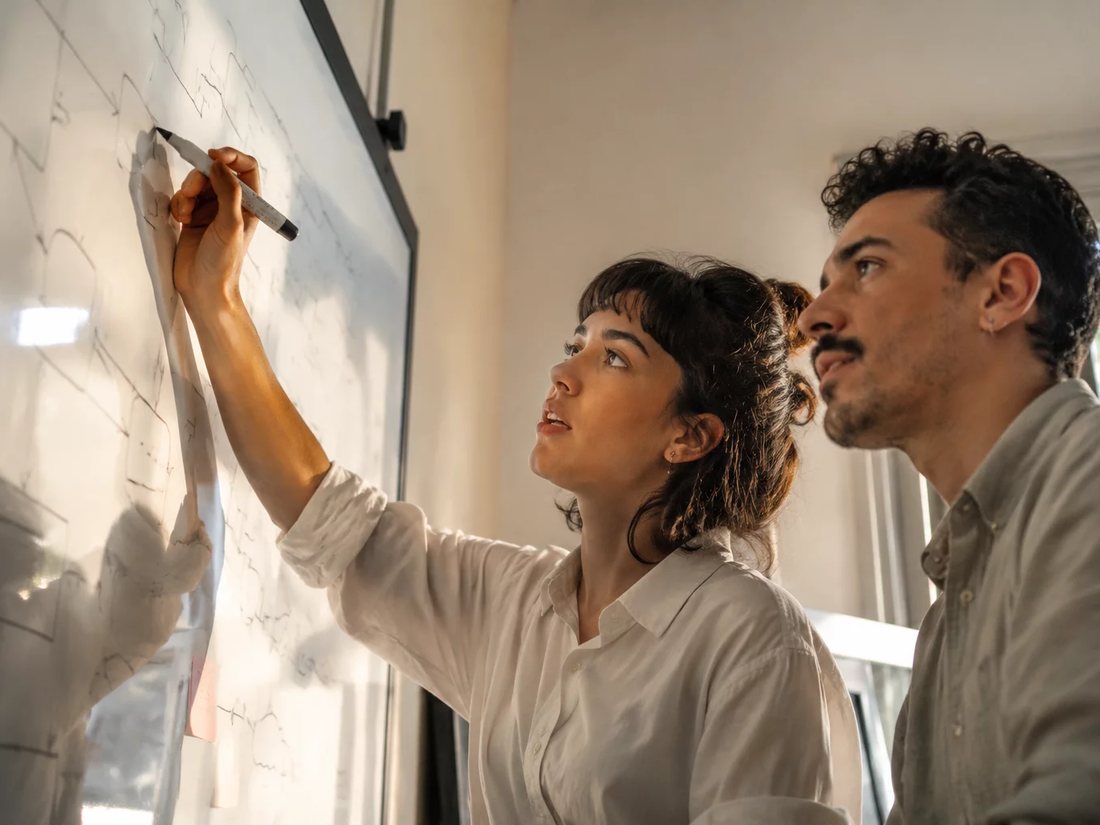 Dois alunos em pé diante do quadro branco, desenhando a ordem de um argumento